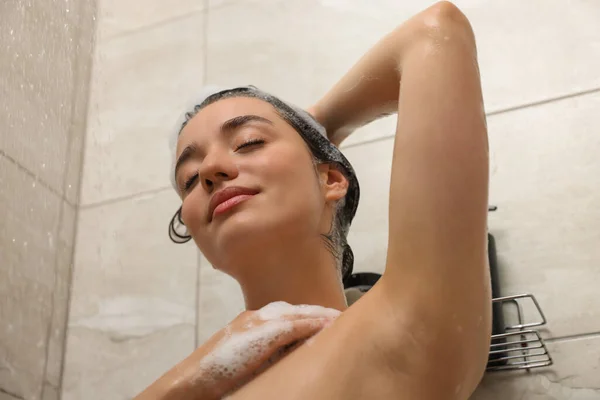 Beautiful woman washing hair with shampoo in shower, low angle view