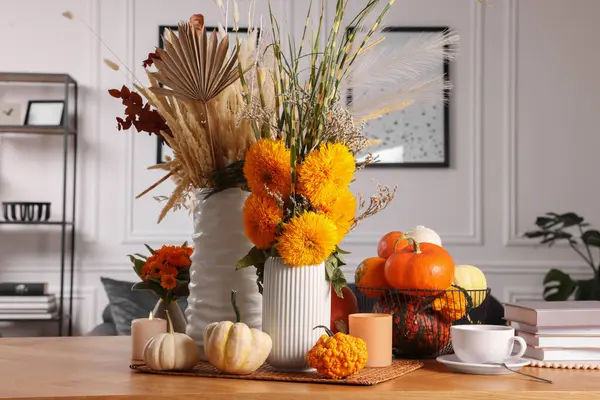 Beautiful autumn composition with bright orange flowers, pumpkins and burning candles on wooden table in room