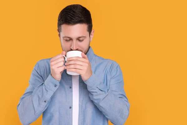 Man drinking from white mug on orange background. Space for text
