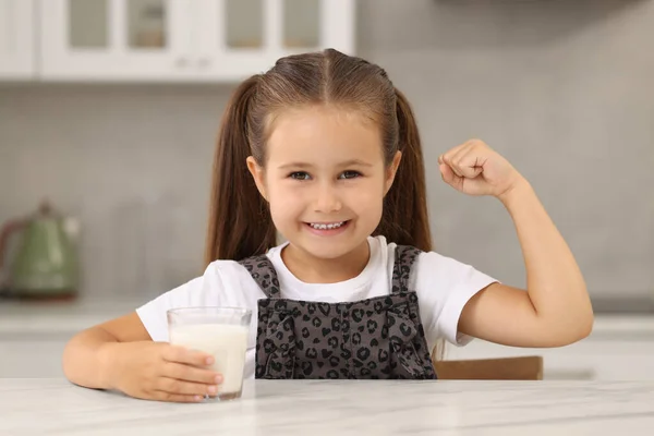 キッチンで白いテーブルで彼女の強さを示す新鮮なミルクのガラスとかわいい少女 — ストック写真