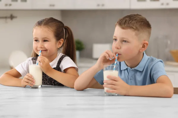 キッチンのホワイトテーブルでメガネから新鮮なミルクを飲むかわいい子供たち — ストック写真