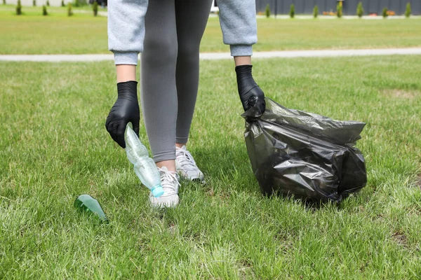 Woman with trash bag picking up glass and plastic bottles outdoors, closeup. Recycling concept