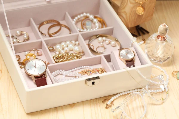 Jewelry box with many different accessories and perfume on wooden table, closeup