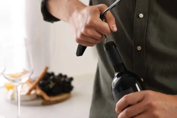 Romantic dinner. Man opening wine bottle with corkscrew in kitchen, closeup and space for text