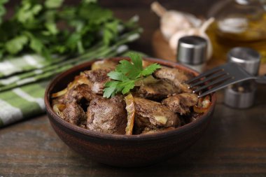 Lezzetli kızarmış tavuk ciğeri soğan ve çatalla ahşap masa, yakın plan.