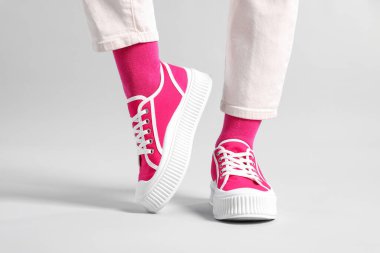 Açık gri arka planda şık, pembe çoraplı, spor ayakkabılı ve pantolonlu kadın, yakın plan.