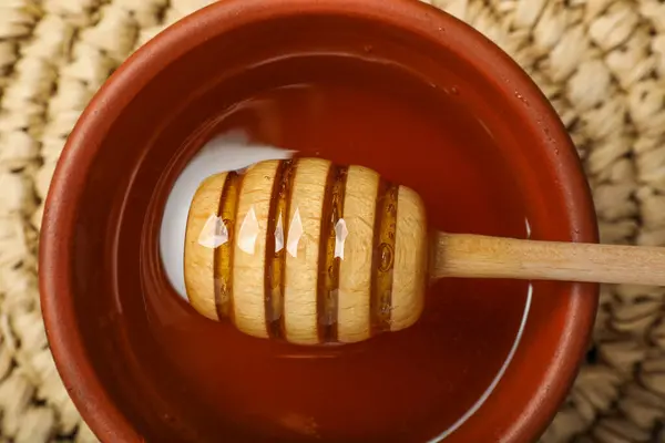 Dipper with honey in bowl on table, top view