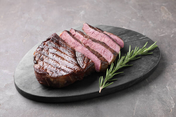 Delicious fried beef meat with rosemary on grey textured table
