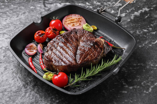 Grill pan with delicious fried beef meat, spices and vegetables on grey textured table