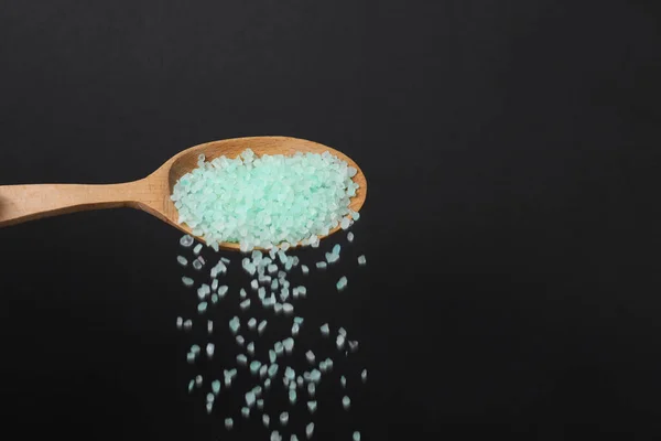 Pouring turquoise sea salt from wooden spoon against black background, closeup. Space for text