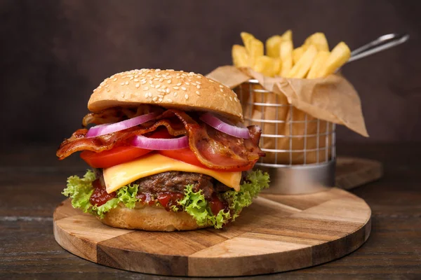 Tasty burger with bacon, vegetables and patty served with french fries on wooden table