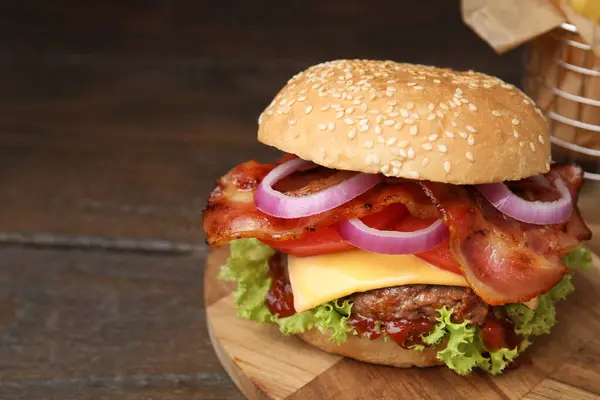 Tasty burger with bacon, vegetables and patty on wooden table, closeup. Space for text