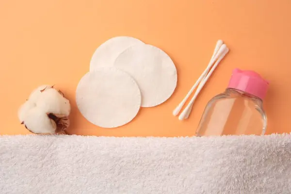 Flat lay composition with makeup remover and cotton flower on pale orange background