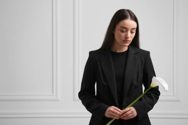 Beyaz duvarın yanında elinde zambak çiçeği olan üzgün kadın, mesaj için yer var. Cenaze töreni.