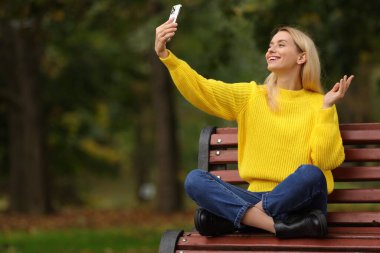 Mutlu kadın sonbahar parkında akıllı telefonuyla görüntülü konuşma yapıyor. Metin için boşluk