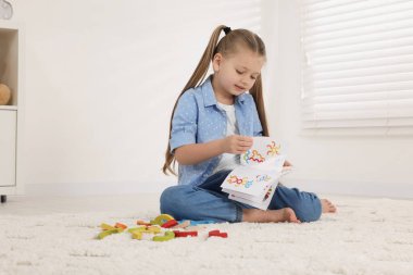 Motor beceri geliştirme. İçerideki renkli ahşap kavislerin yanında talimat okuyan bir kız. Metin için boşluk