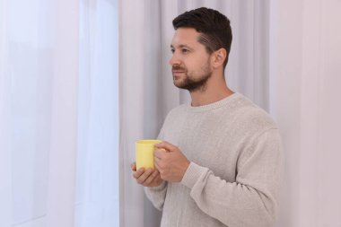 Evde elinde sarı seramik bardak tutan bir adam. Metin için boşluk