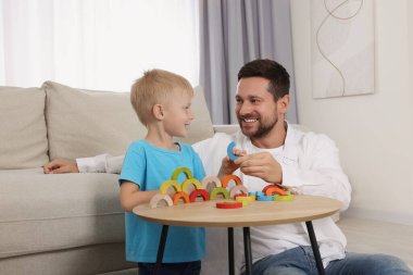 Motor beceri geliştirme. Mutlu baba, oğlunun odasındaki kahve masasında renkli ahşap kavislerle oynamasına yardım ediyor.