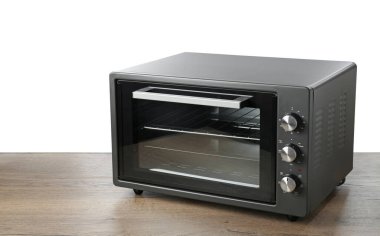 Ahşap masada beyaz zemine karşı bir elektrikli fırın.