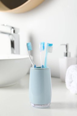 Banyodaki beyaz tezgahta plastik diş fırçaları olan tutucu.