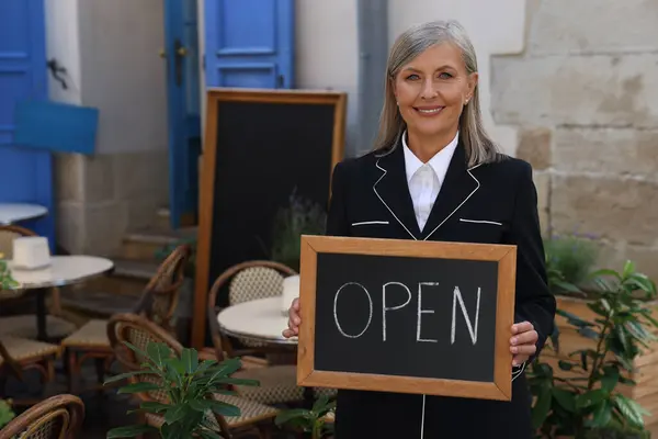 Happy business owner holding open sign near her cafe outdoors, space for text
