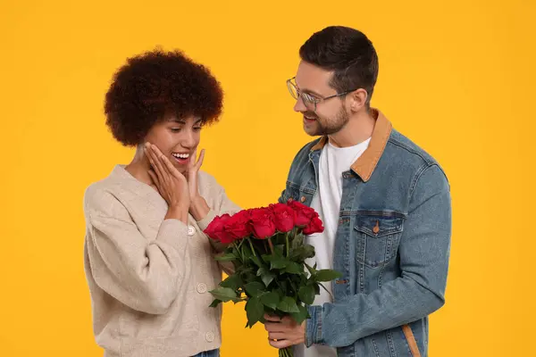 International dating. Handsome man presenting roses to his beloved woman on orange background