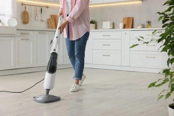 Woman cleaning floor with steam mop in kitchen at home, closeup. Space for text