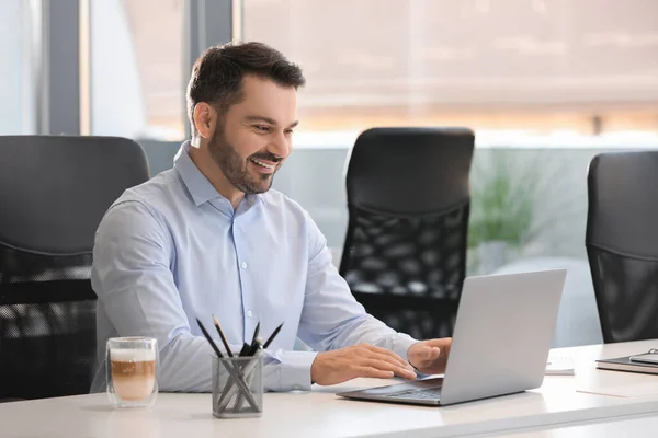 Happy man using modern laptop at white desk in office