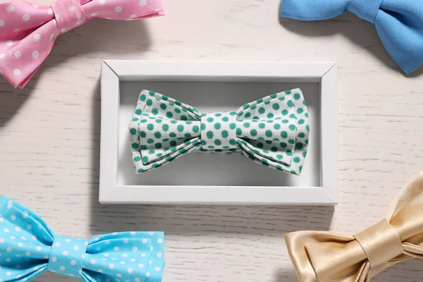 Stylish color bow ties on white wooden table, flat lay