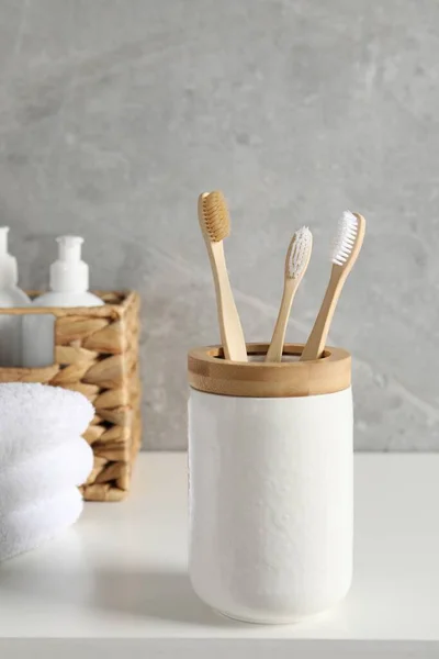 Bamboo toothbrushes in holder, towels and cosmetic products on white countertop