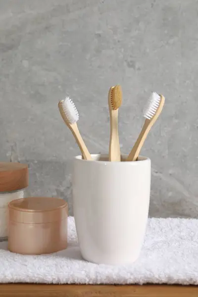 Bamboo toothbrushes in holder, towel and cosmetic products on wooden table
