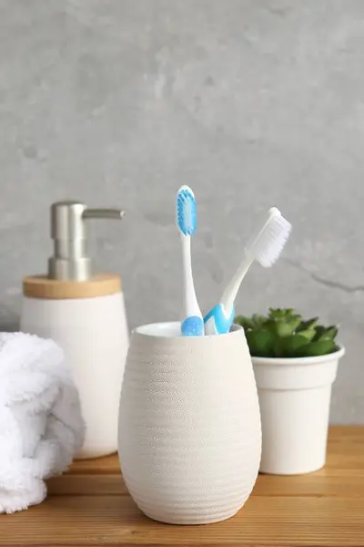 Plastic toothbrushes in holder, towel, potted plant and cosmetic product on wooden table