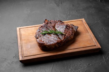 Lezzetli kızarmış biftekli ahşap tahta tahta ve gri desenli masada biberiye.