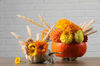 Dekoratif balkabakları, güzel çiçekler ve tahta masa üzerinde çiviler beyaz tuğla duvara karşı.