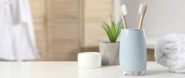 Bambu diş fırçaları, havlu, ev bitkisi ve kişisel bakım ürünleri banyodaki beyaz masada, mesaj için yer var. Pankart tasarımı
