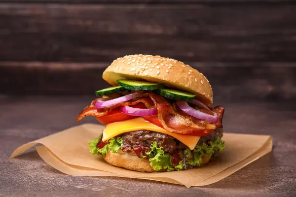 Tasty burger with bacon, vegetables and patty on textured table