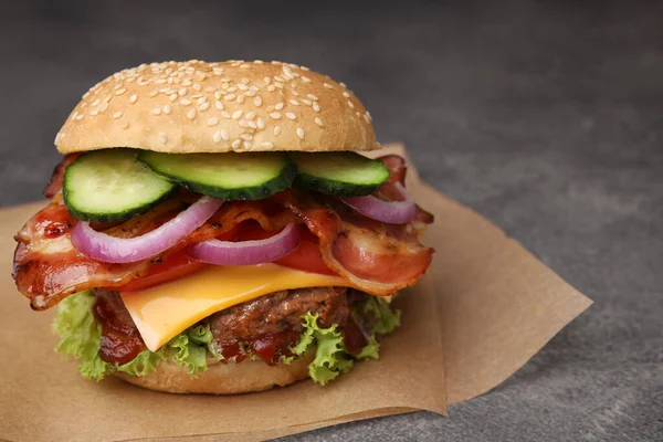 Tasty burger with bacon, vegetables and patty on textured table, closeup. Space for text
