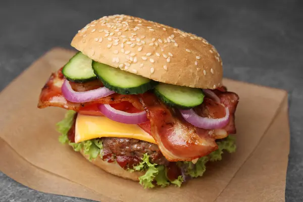 Tasty burger with bacon, vegetables and patty on table, closeup