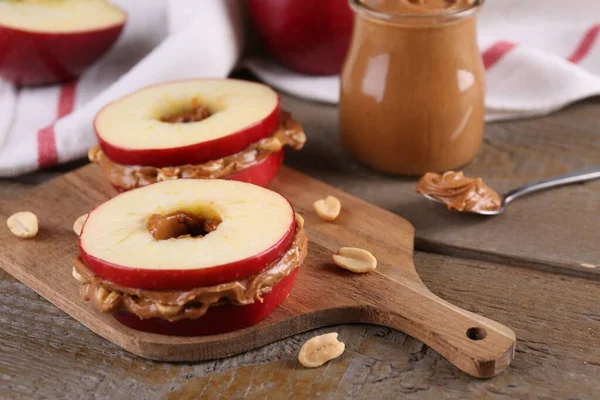 Slices of fresh apple with peanut butter and nuts on wooden table, closeup