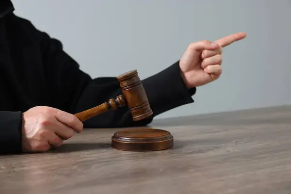 stock image Judge with gavel sitting at wooden table against light grey background, closeup