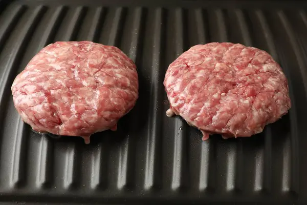 Fresh raw hamburger patties on electric grill, closeup