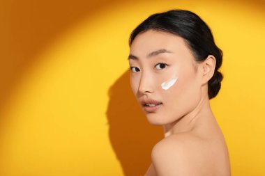 Güneş ışığı altında güzel bir genç kadın. Yüzünde turuncu arka planda güneş kremi var. Mesaj için yer var.