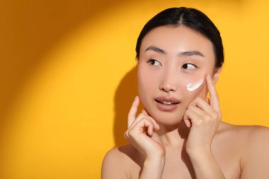 Güneş ışığı altında güzel bir genç kadın. Yüzünde turuncu arka planda güneş kremi var. Mesaj için yer var.