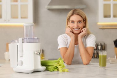 Mutfakta meyve sıkacağı ve taze kereviz ile masada mutlu bir kadın. Metin için boşluk