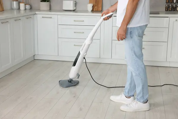 Man cleaning floor with steam mop in kitchen at home, closeup