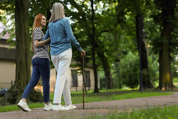 Senior lady with walking cane and young woman in park, back view. Space for text