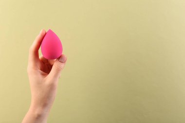 Açık sarı arka planda pembe makyaj süngeri olan kadın, yakın plan. Metin için boşluk