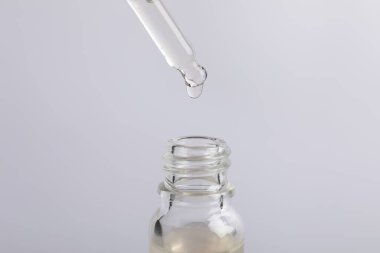 Açık gri arka planda pipetten şişeye kozmetik serumu damlatıyor