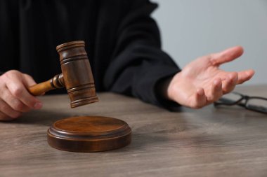 Tokmaklı yargıç, açık gri arka planda, ahşap masada oturuyor, yakın plan.