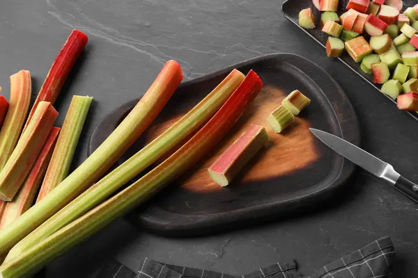 stock image Whole and cut rhubarb stalks and knife on black table, flat lay